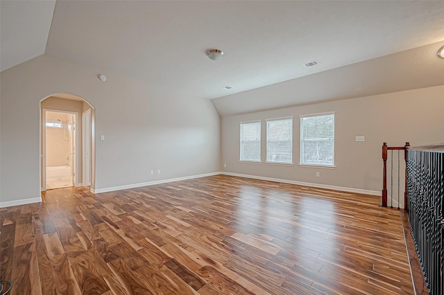 unfurnished living room with arched walkways, lofted ceiling, visible vents, wood finished floors, and baseboards