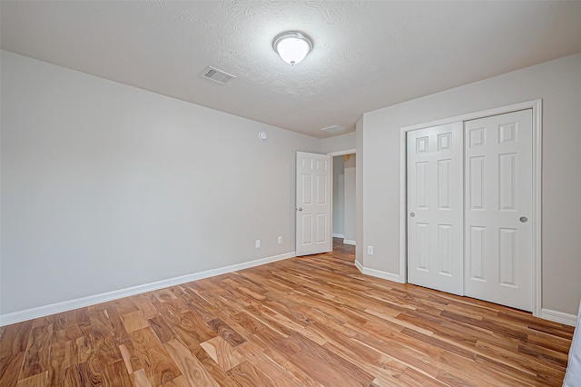 unfurnished bedroom featuring a closet, visible vents, light wood-style floors, a textured ceiling, and baseboards