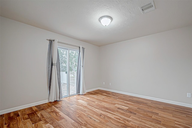 spare room featuring a textured ceiling, light wood-type flooring, visible vents, and baseboards