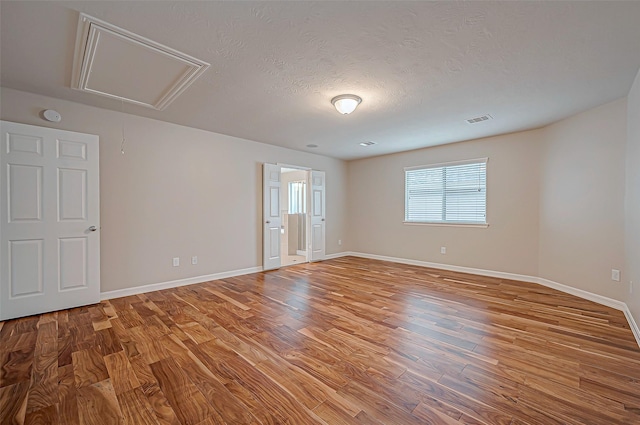 empty room featuring baseboards, light wood finished floors, visible vents, and attic access