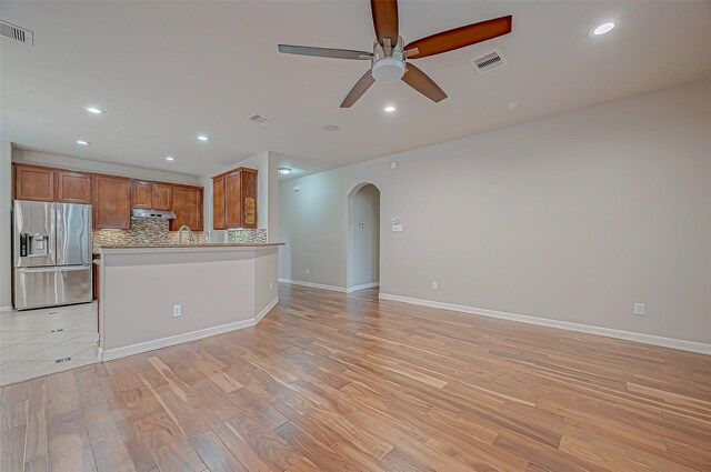 interior space with backsplash, ceiling fan, kitchen peninsula, stainless steel refrigerator with ice dispenser, and light hardwood / wood-style flooring