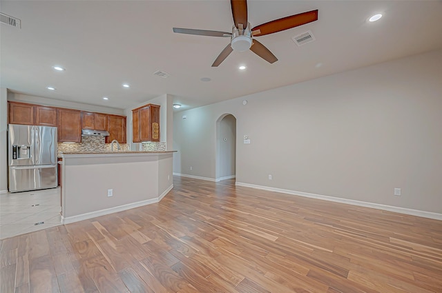 unfurnished living room featuring arched walkways, light wood-type flooring, visible vents, and a ceiling fan