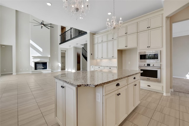 kitchen with light tile patterned floors, appliances with stainless steel finishes, light stone countertops, a kitchen island, and decorative light fixtures