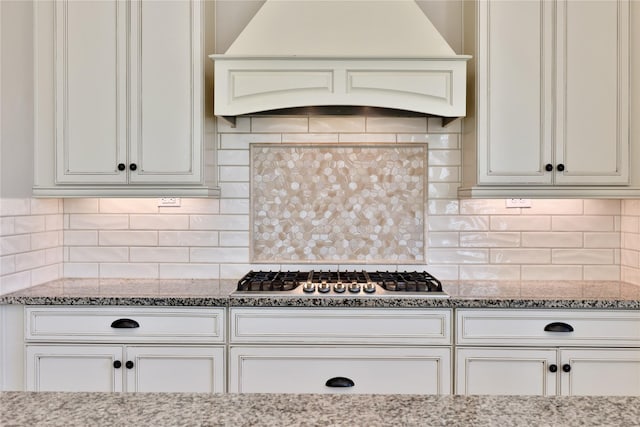 kitchen with white cabinetry, backsplash, light stone countertops, custom exhaust hood, and stainless steel gas stovetop