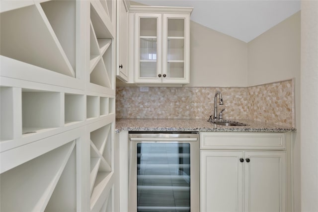 bar with tasteful backsplash, sink, white cabinets, beverage cooler, and light stone countertops