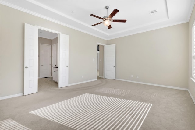 unfurnished bedroom with ceiling fan, ornamental molding, a tray ceiling, and light carpet