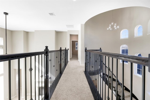 hallway with light colored carpet and a chandelier