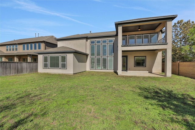 back of house with ceiling fan, a balcony, a patio area, and a lawn