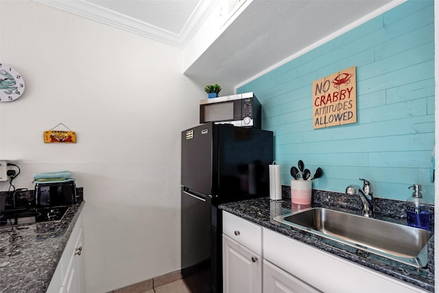 kitchen with wooden walls, white cabinetry, sink, ornamental molding, and black fridge