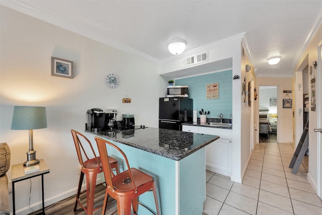 kitchen with black refrigerator, white cabinetry, sink, a kitchen bar, and kitchen peninsula