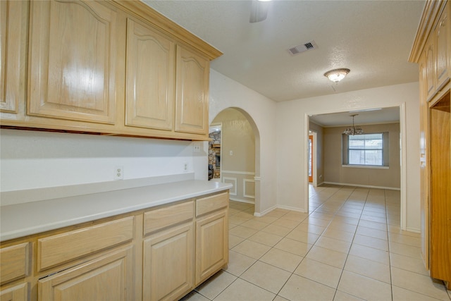 kitchen with light tile patterned floors, ceiling fan with notable chandelier, a textured ceiling, decorative light fixtures, and light brown cabinets