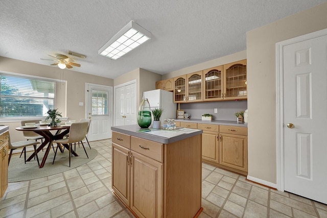 kitchen with light brown cabinetry, a textured ceiling, white fridge, a kitchen island, and ceiling fan