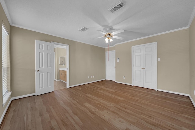 unfurnished bedroom featuring ceiling fan, connected bathroom, ornamental molding, a textured ceiling, and light wood-type flooring