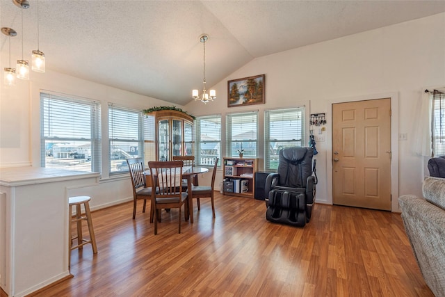 dining space with lofted ceiling, a healthy amount of sunlight, an inviting chandelier, and wood finished floors