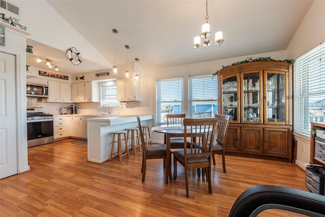 dining room featuring light wood-style floors, vaulted ceiling, and a notable chandelier