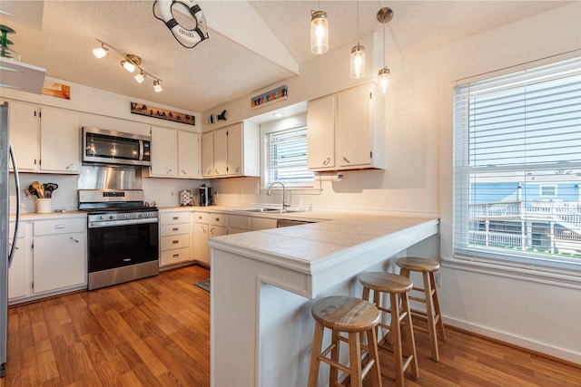 kitchen with stainless steel appliances, a peninsula, white cabinetry, and pendant lighting