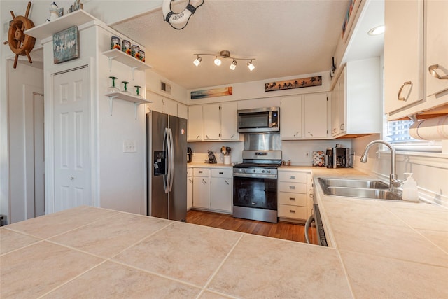 kitchen with stainless steel appliances, a sink, tile countertops, and open shelves