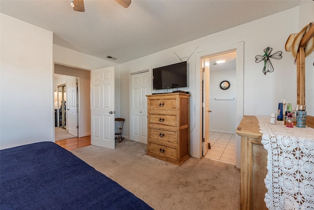 bedroom with visible vents, ceiling fan, light carpet, and a textured ceiling