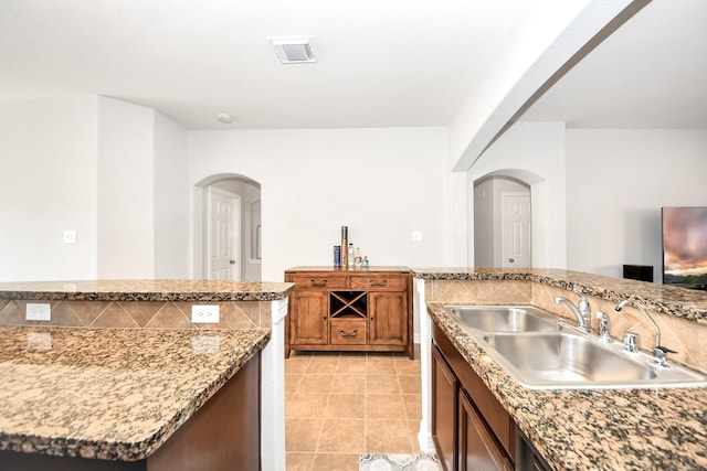 kitchen featuring sink, light tile patterned floors, light stone countertops, and an island with sink