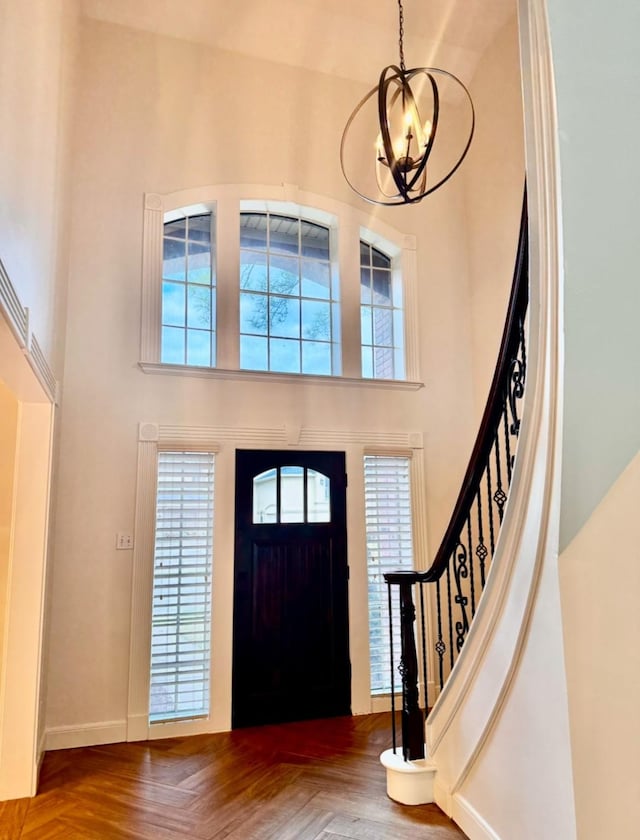 foyer entrance with parquet flooring, a chandelier, and a towering ceiling