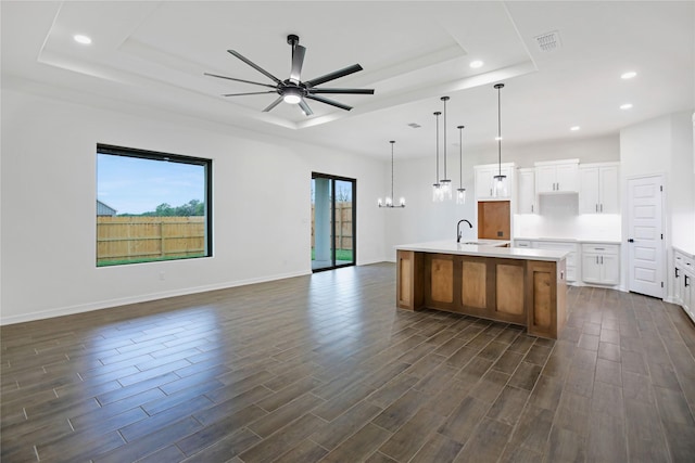 kitchen featuring a spacious island, a tray ceiling, white cabinets, ceiling fan with notable chandelier, and decorative light fixtures