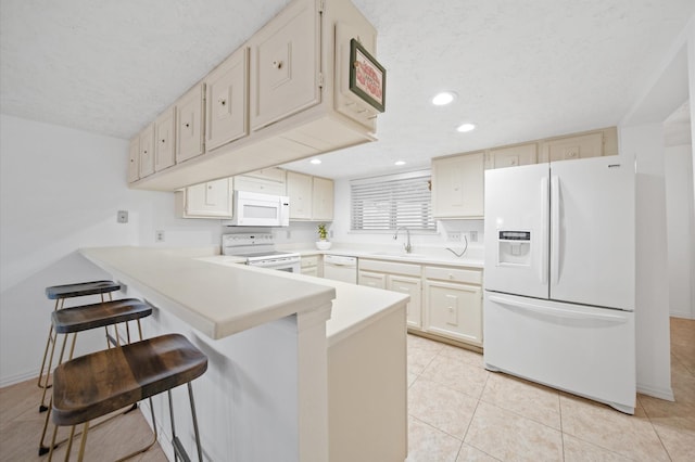 kitchen featuring light tile patterned flooring, a breakfast bar, sink, kitchen peninsula, and white appliances