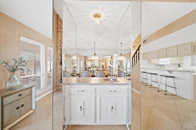 kitchen with a kitchen island, decorative light fixtures, white cabinetry, sink, and light tile patterned floors