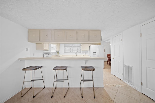 kitchen with light tile patterned floors, white appliances, a breakfast bar, a textured ceiling, and kitchen peninsula