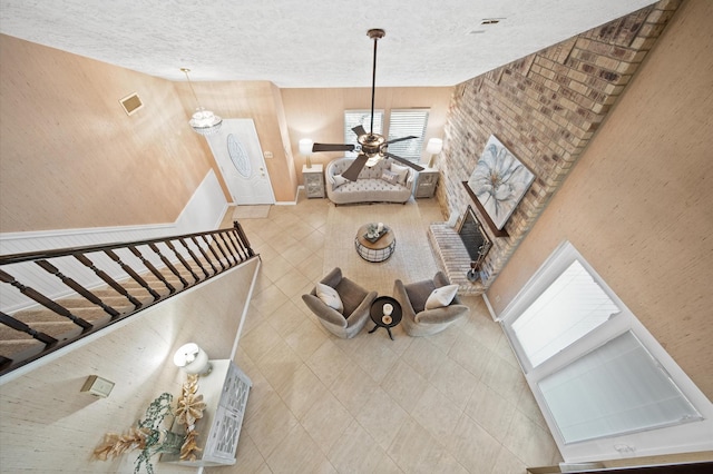 living room with a high ceiling, ceiling fan, a brick fireplace, and a textured ceiling