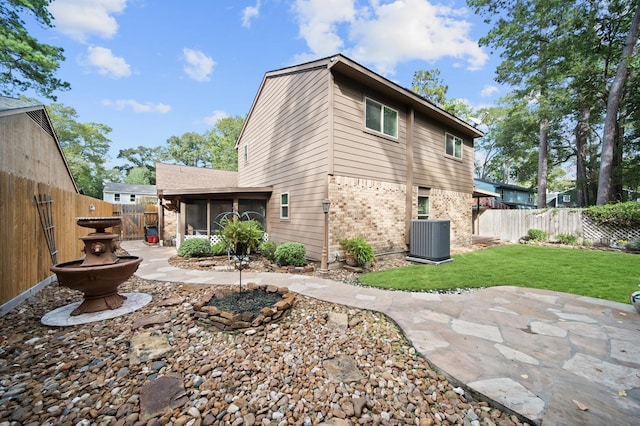 rear view of house featuring a lawn, a sunroom, central AC, and a patio area