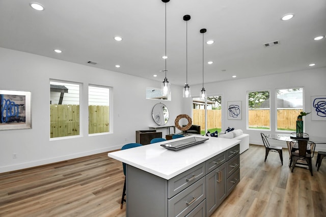 kitchen with light hardwood / wood-style flooring, gray cabinetry, a kitchen breakfast bar, a center island, and decorative light fixtures