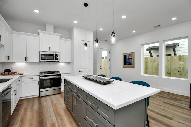 kitchen with white cabinetry, stainless steel appliances, decorative light fixtures, and a kitchen island