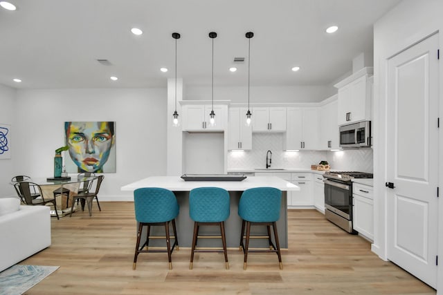 kitchen featuring white cabinetry, decorative light fixtures, a kitchen island, and appliances with stainless steel finishes