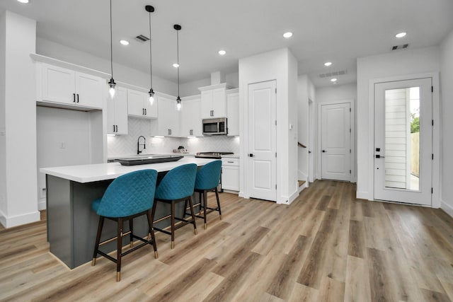 kitchen featuring a breakfast bar area, a center island, pendant lighting, light hardwood / wood-style floors, and white cabinets