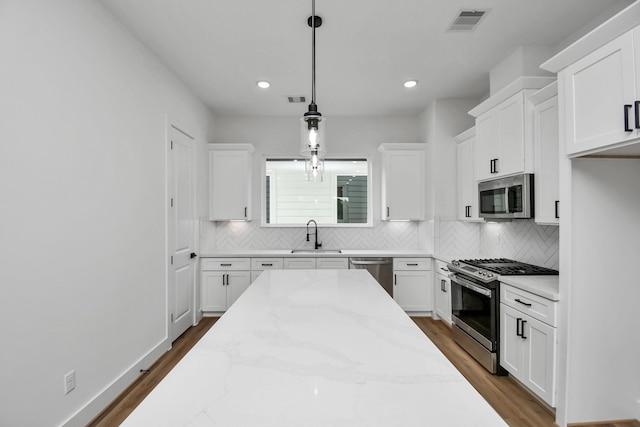 kitchen with sink, pendant lighting, stainless steel appliances, light stone countertops, and white cabinets