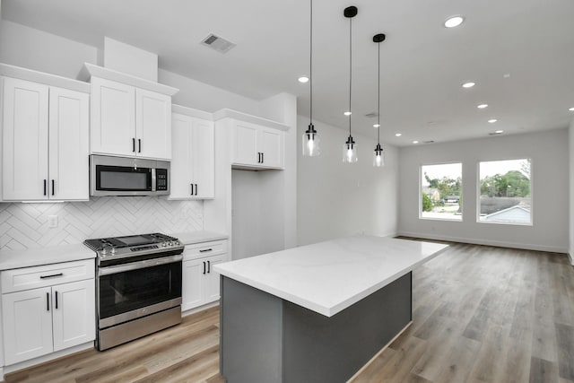 kitchen with stainless steel appliances, white cabinetry, hanging light fixtures, and backsplash