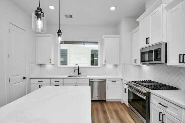 kitchen featuring sink, white cabinetry, decorative light fixtures, stainless steel appliances, and light stone countertops