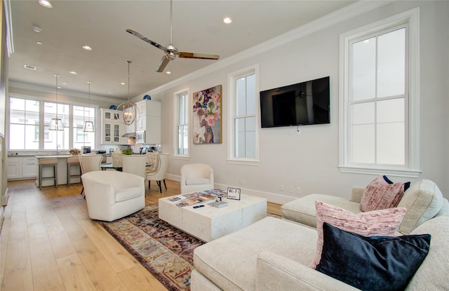 living room with sink, crown molding, light hardwood / wood-style flooring, and ceiling fan with notable chandelier