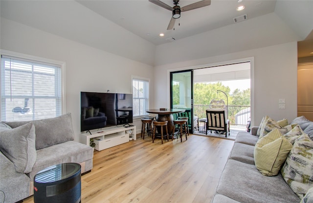 living room with light hardwood / wood-style floors, a raised ceiling, and ceiling fan