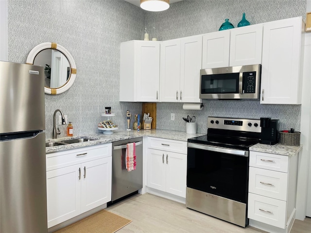 kitchen featuring light stone counters, appliances with stainless steel finishes, sink, and white cabinets