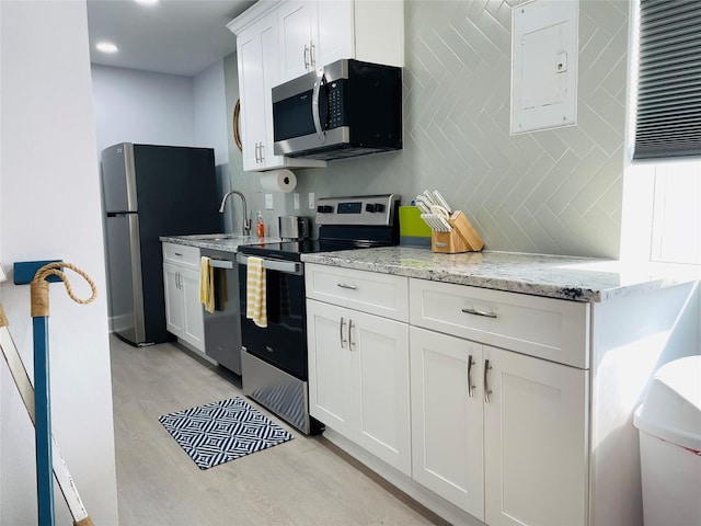 kitchen featuring white cabinetry, decorative backsplash, stainless steel appliances, light stone countertops, and light wood-type flooring