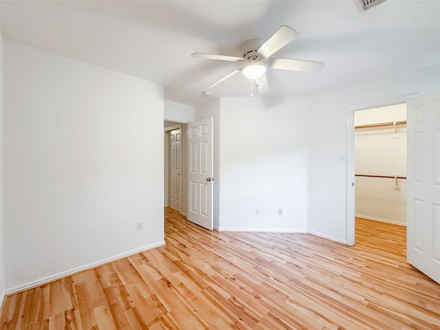 unfurnished bedroom with a closet, a spacious closet, ceiling fan, and light hardwood / wood-style flooring