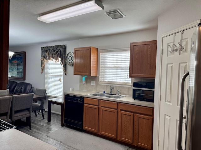 kitchen with sink, stainless steel refrigerator, black dishwasher, and light wood-type flooring