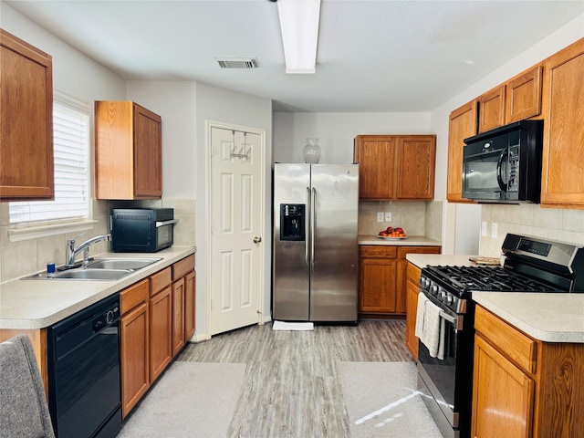 kitchen with sink, decorative backsplash, black appliances, and light wood-type flooring