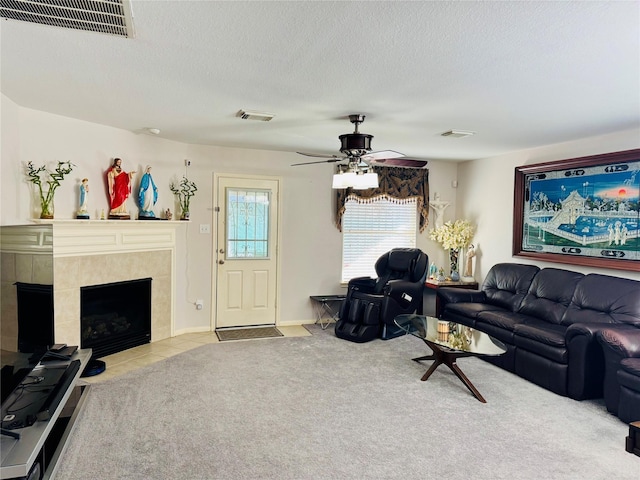 living room with ceiling fan, a tile fireplace, light carpet, and a textured ceiling