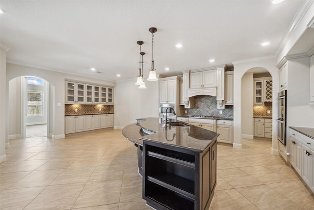 kitchen with pendant lighting, sink, dark stone countertops, stainless steel appliances, and a center island with sink