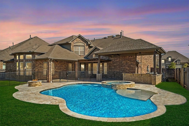 pool at dusk featuring an in ground hot tub, an outdoor fire pit, a yard, and a patio area