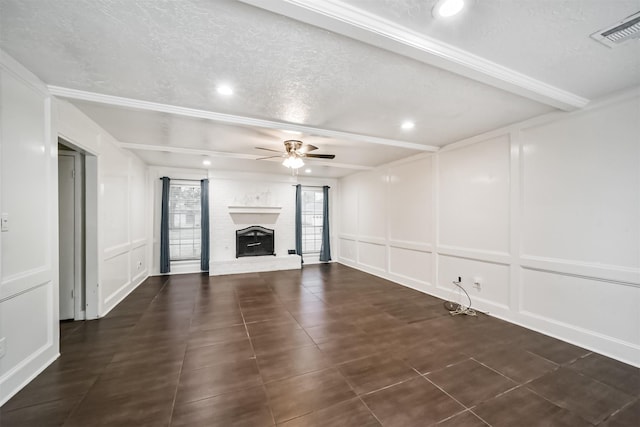 unfurnished living room featuring beam ceiling, ceiling fan, a brick fireplace, and a textured ceiling