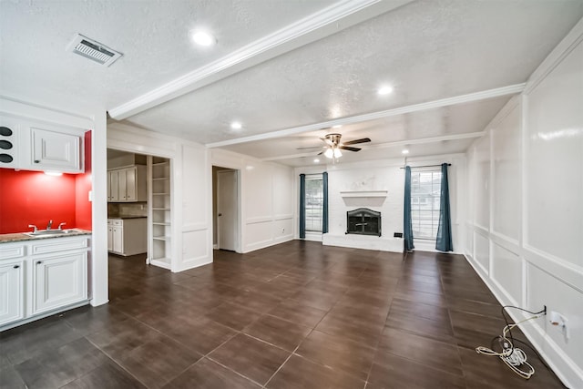 unfurnished living room featuring sink, ceiling fan, a textured ceiling, a brick fireplace, and beamed ceiling