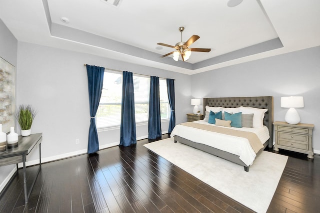 bedroom featuring dark hardwood / wood-style flooring, a tray ceiling, and ceiling fan